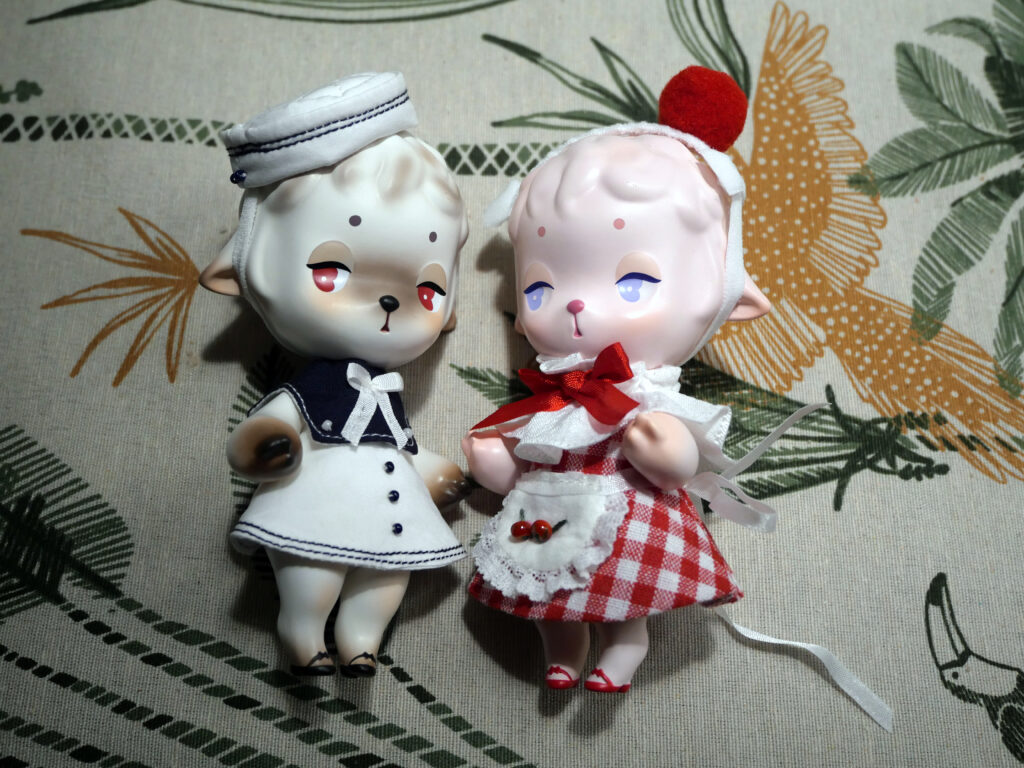 The White and black sheep is dressed up in the sailor outfit while the pink sheep is wearing the red candy apple outfit.