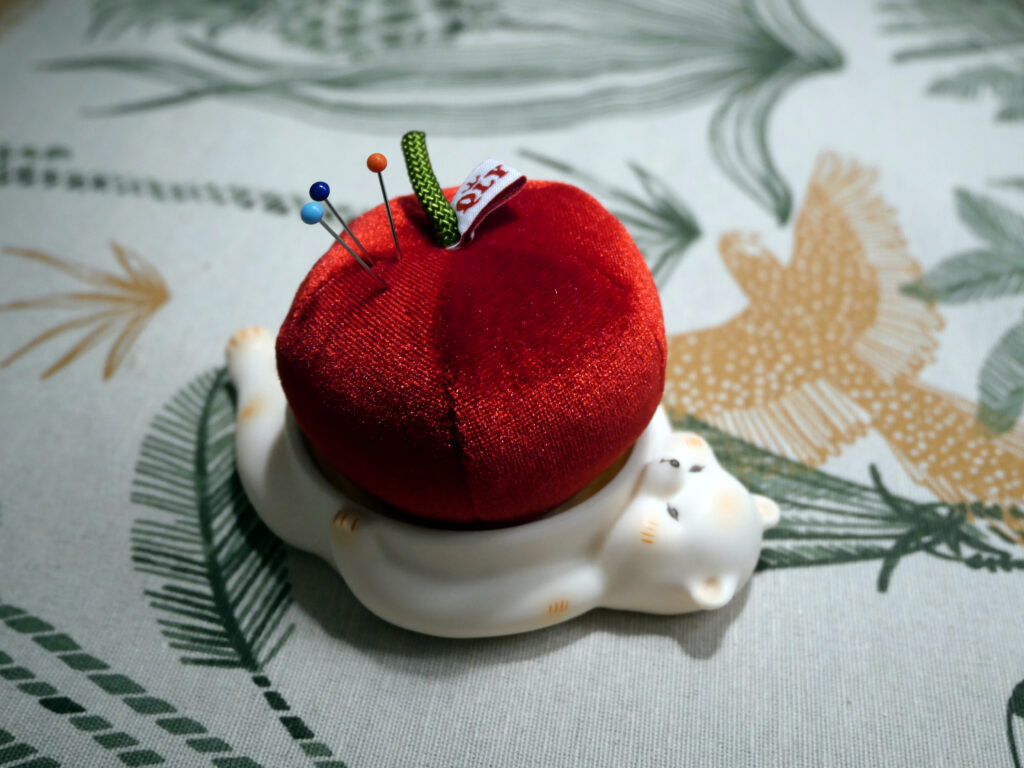 The bear shaped pin cushion holder is shown from the side while three pins are sticking out of the red apple pin cushion