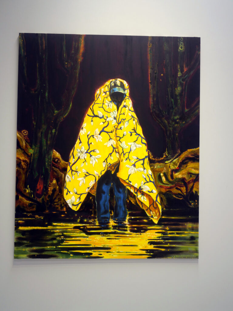 A man draped with a yellow cape traveling through marshlands. The yellow is so vibrant that it makes the cape look like he is someone royal. - The Mexican